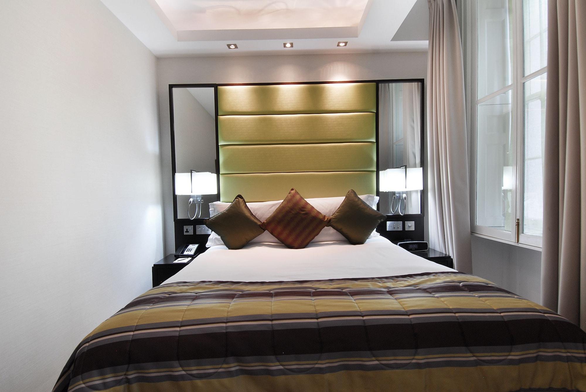 Montcalm Brewery Townhouse Hotel Лондон Екстериор снимка The photo shows a stylishly decorated bedroom. The bed is centered in the room, featuring a white comforter with a plaid pattern in shades of brown and green. There are three decorative pillows on the bed, two in shades of brown and one in dark green