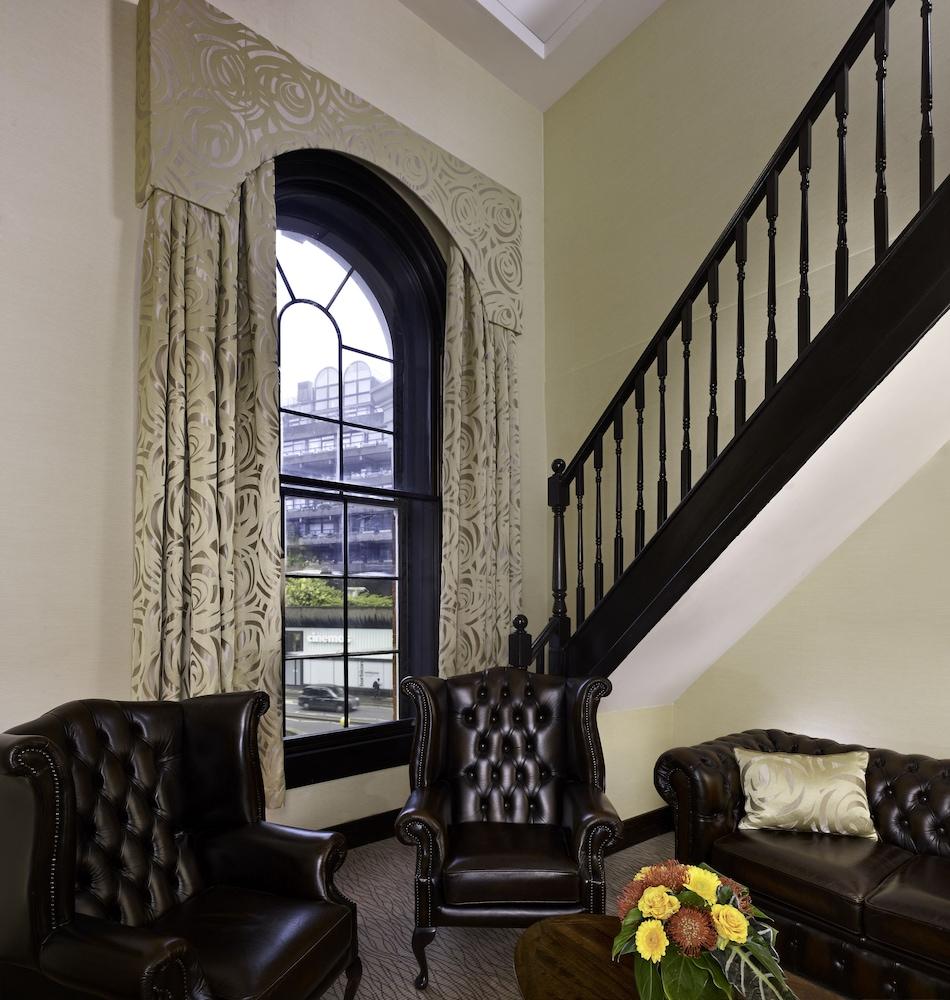 Montcalm Brewery Townhouse Hotel Лондон Екстериор снимка The photo shows a cozy interior space featuring two elegant leather armchairs placed near a large, ornate window with arched top and decorative curtains. The wall is painted in a muted color, enhancing the warmth of the room. A staircase with black s