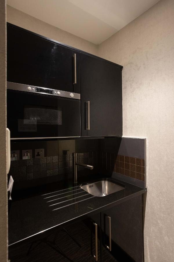 Montcalm Brewery Townhouse Hotel Лондон Екстериор снимка The photo shows a modern kitchen setup with a dark color scheme. It features:

- A built-in microwave oven situated above a countertop.
- A sleek black cabinet beneath the microwave, which likely stores kitchen items.
- A stainless steel sink placed 