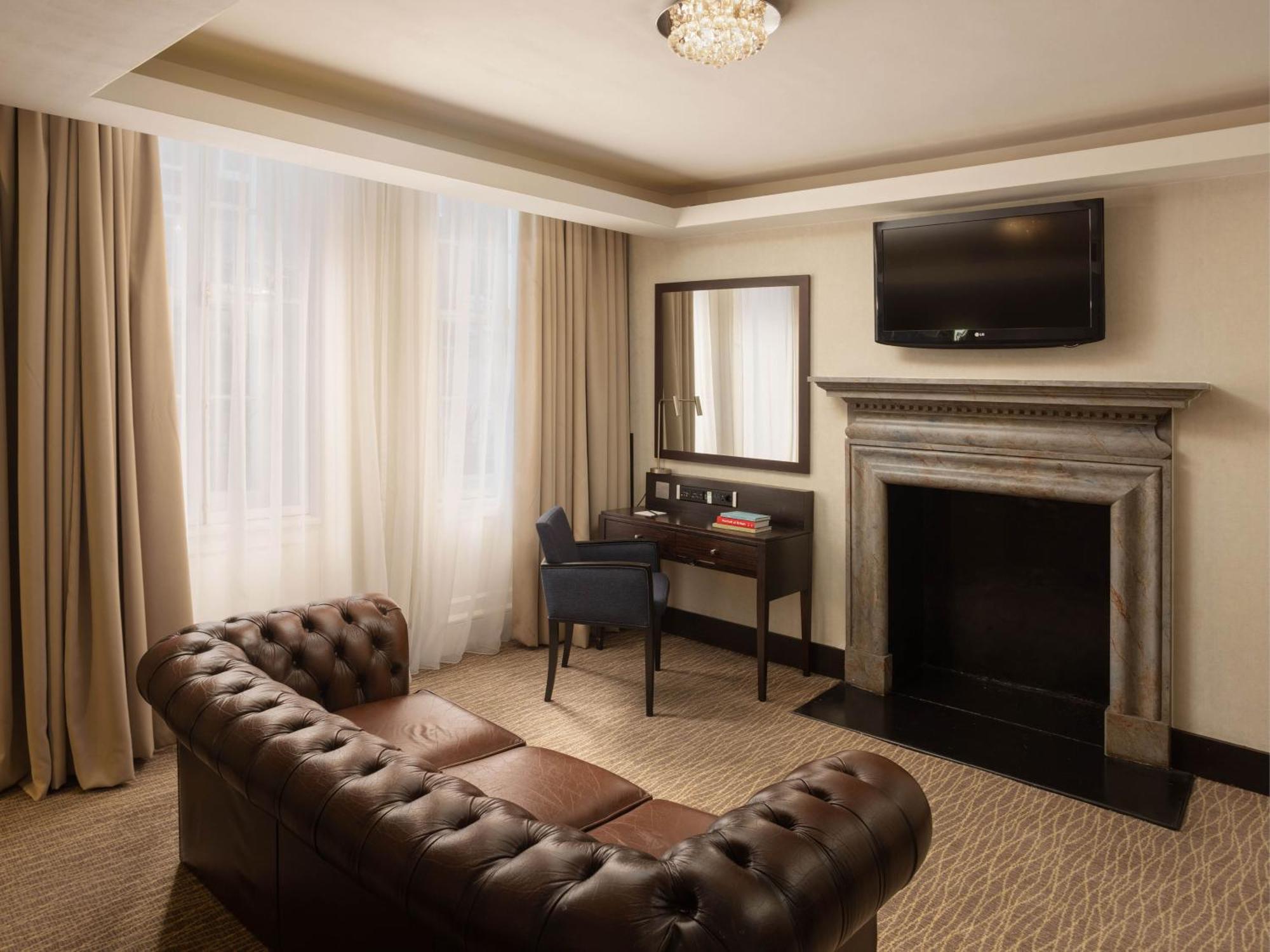 Montcalm Brewery Townhouse Hotel Лондон Екстериор снимка The photo shows a cozy and elegantly designed room. There is a comfortable brown leather sofa with tufted detailing. A small desk and chair are positioned near a mirror, providing a space for work or personal grooming. On the wall, a flat-screen TV i