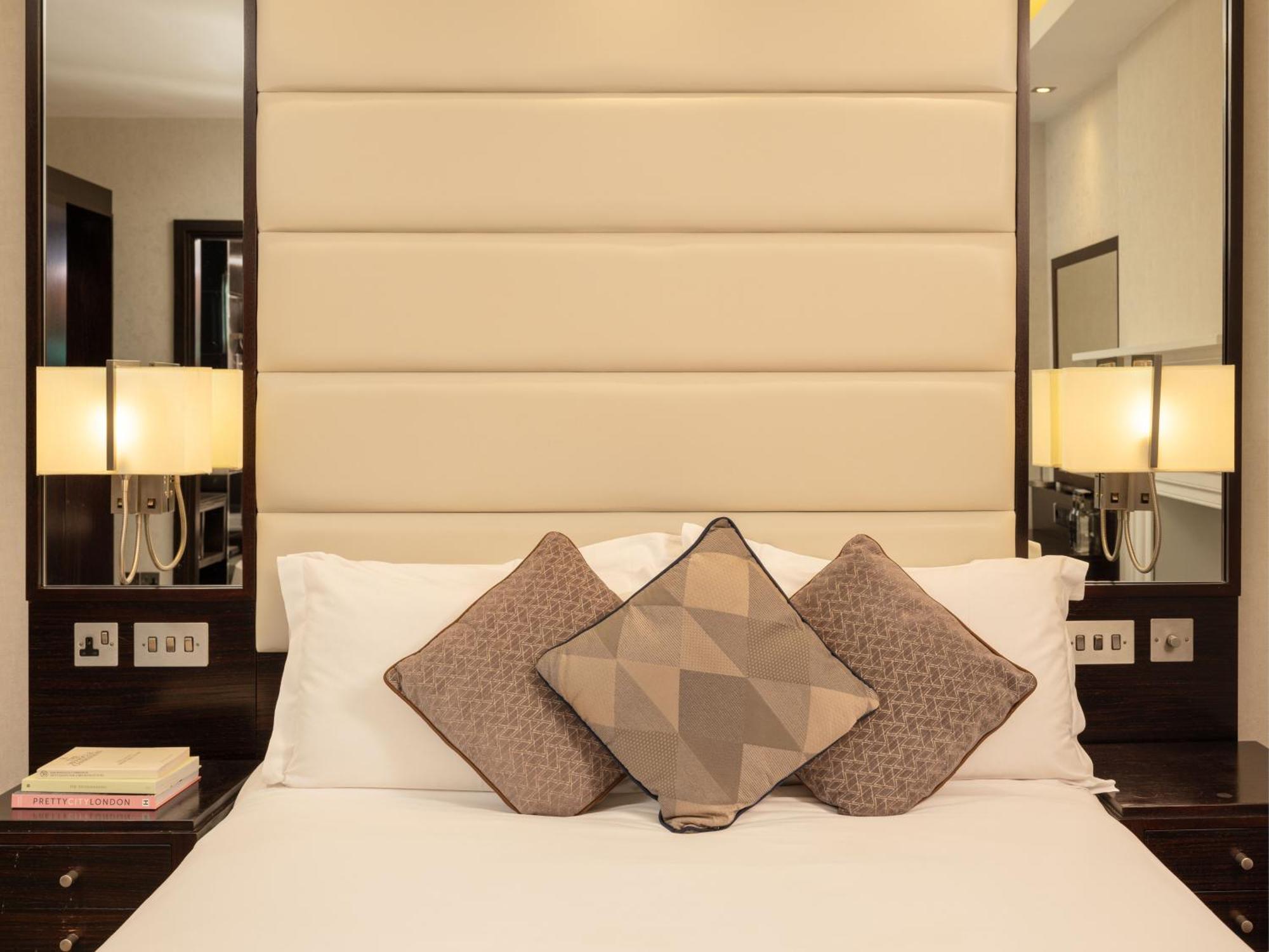 Montcalm Brewery Townhouse Hotel Лондон Екстериор снимка The image shows a cozy bedroom setting. The bed features a headboard upholstered in a light beige fabric. It is adorned with three decorative pillows in varying patterns and colors, placed on white bedding. On either side of the bed, there are modern