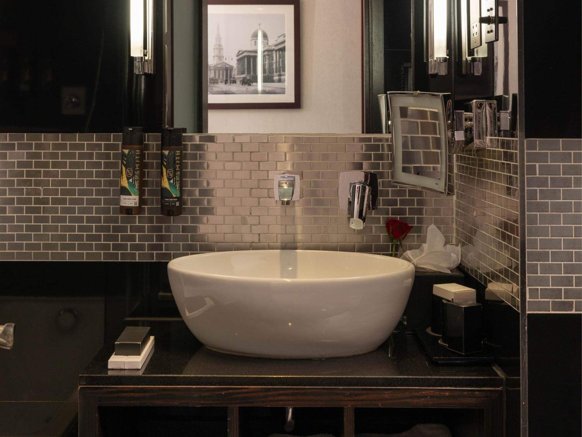 Montcalm Brewery Townhouse Hotel Лондон Екстериор снимка The photo shows a modern bathroom with a stylish design. It features a large, round white sink placed on a dark wooden vanity. The walls are adorned with a mix of gray and silver tile, creating a sleek and contemporary look. Above the sink, there is 