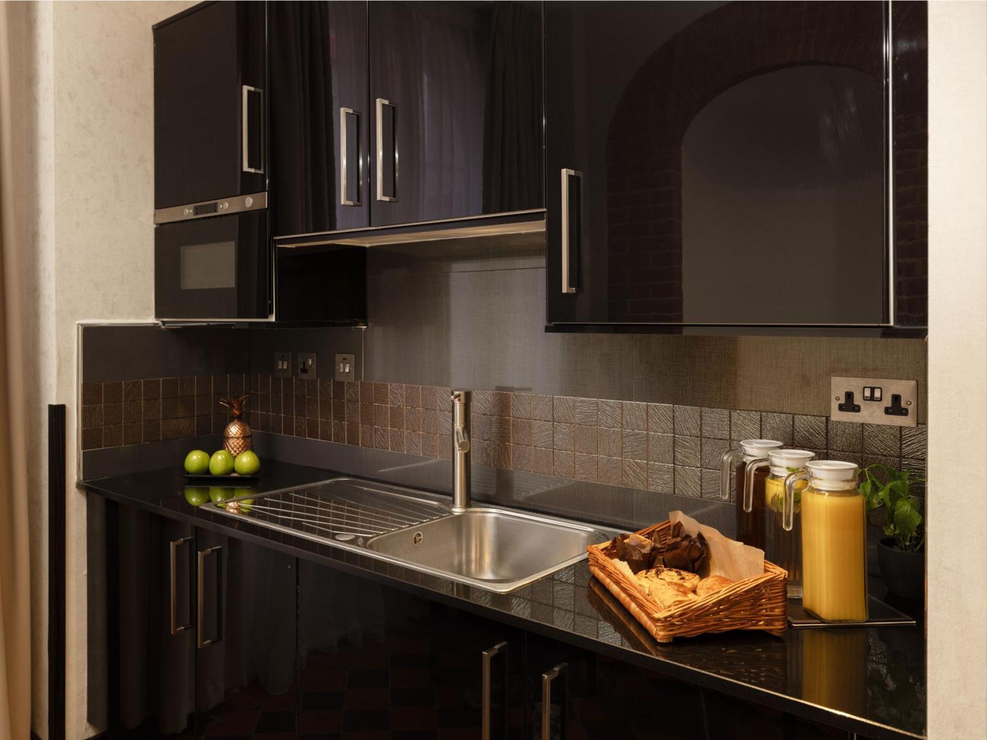 Montcalm Brewery Townhouse Hotel Лондон Екстериор снимка The photo shows a modern kitchen with sleek black cabinetry and a glossy finish. The kitchen features a stainless steel sink with a contemporary faucet, set against a dark, textured countertop. Above the counter, there are cabinets that match the cou