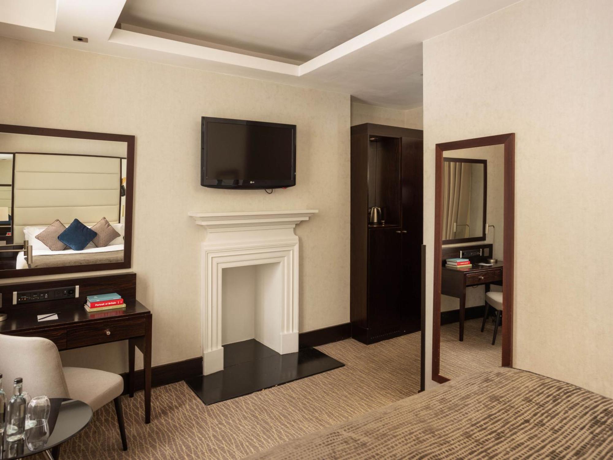 Montcalm Brewery Townhouse Hotel Лондон Екстериор снимка The photo depicts a stylish hotel room. It features a double bed, a large flat-screen TV mounted on the wall, and a decorative fireplace. There is a wooden desk with a chair beside it, as well as a mirror hanging on the wall. The decor is modern and 