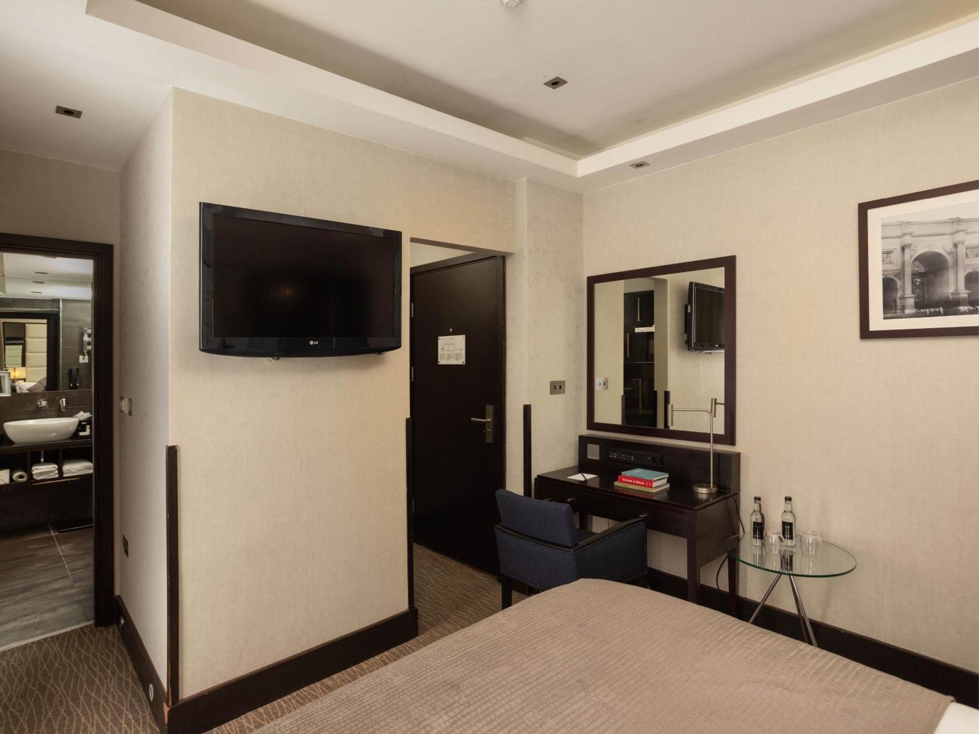 Montcalm Brewery Townhouse Hotel Лондон Екстериор снимка The photo shows a hotel room with a modern and minimalist design. On the left, there's a wall-mounted flat-screen TV. In the center, there's a bed with a neutral-colored bedspread. To the right of the bed, there is a small desk with a mirror above it