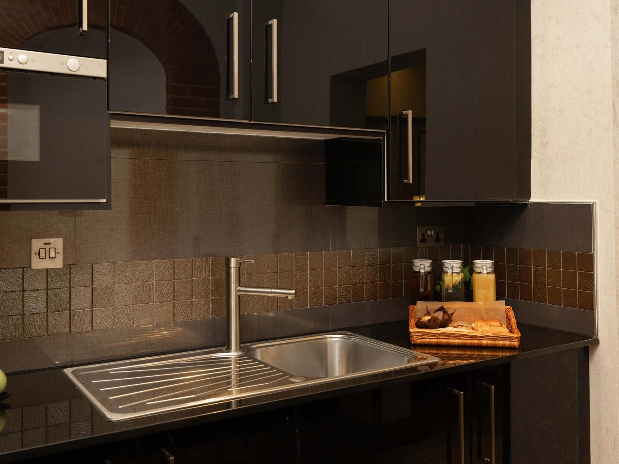 Montcalm Brewery Townhouse Hotel Лондон Екстериор снимка The photo shows a modern kitchen with a sleek design. It features dark cabinetry with a glossy finish and stainless steel handles. There is a stainless steel sink with a simple faucet, and a countertop made of black material. Above the sink, there ar