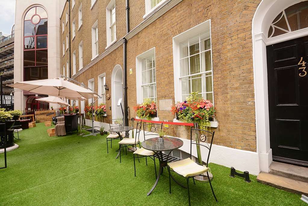 Montcalm Brewery Townhouse Hotel Лондон Екстериор снимка The photo depicts a charming outdoor area in front of a building with a warm, textured brick facade. There is a neatly maintained lawn, likely made of artificial grass, and several small round tables with chairs are arranged outside. Flower pots with