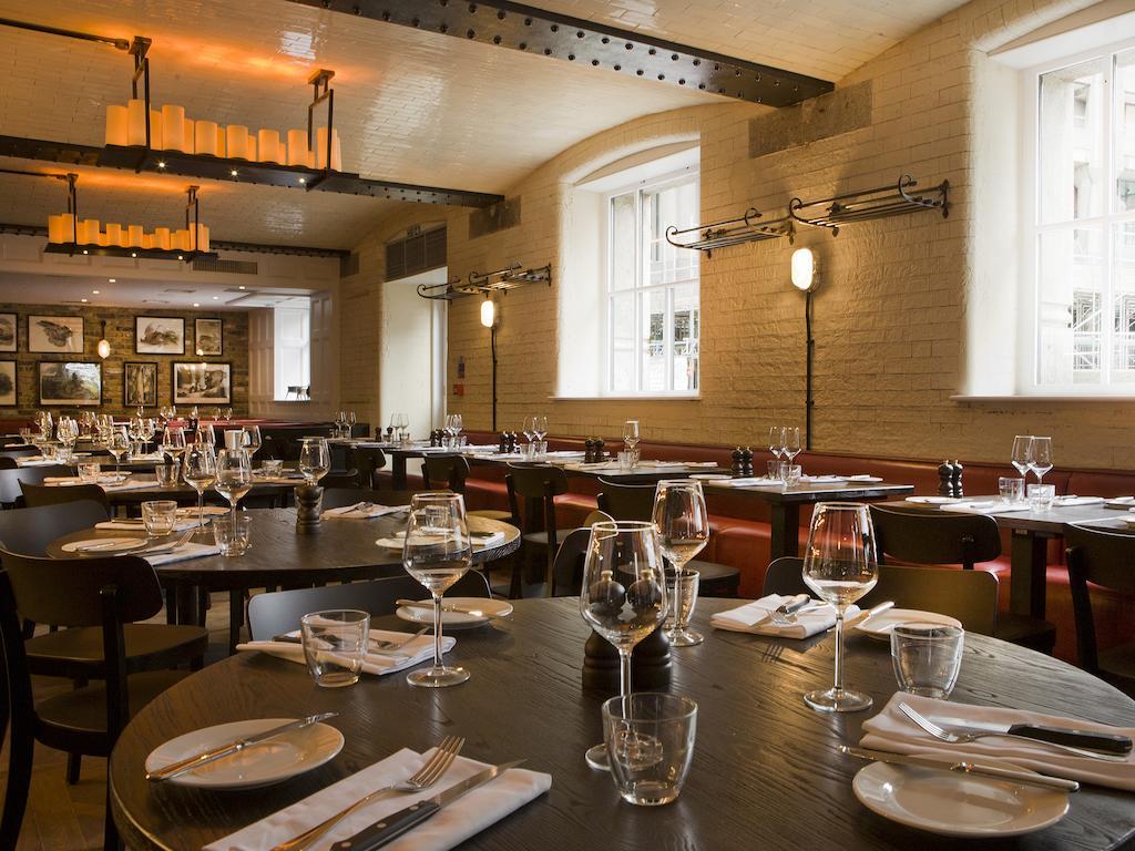Montcalm Brewery Townhouse Hotel Лондон Екстериор снимка The photo shows a restaurant interior featuring a warm and inviting atmosphere. It has several round wooden tables set for dining, each with neatly arranged plates, utensils, and glasses. The lighting is soft, with overhead fixtures providing a cozy 