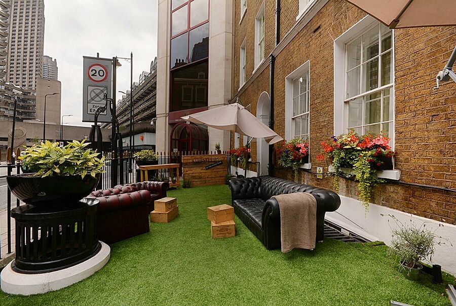 Montcalm Brewery Townhouse Hotel Лондон Екстериор снимка The photo depicts a charming outdoor space, likely a patio or garden area. It features two comfortable-looking leather sofas, one of which is a deep burgundy color, placed on a green artificial lawn. There are wooden crates that could serve as side t